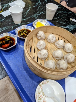 soup dumplings in a basket on a tray with sweet soy sauce and spicy soy sauce